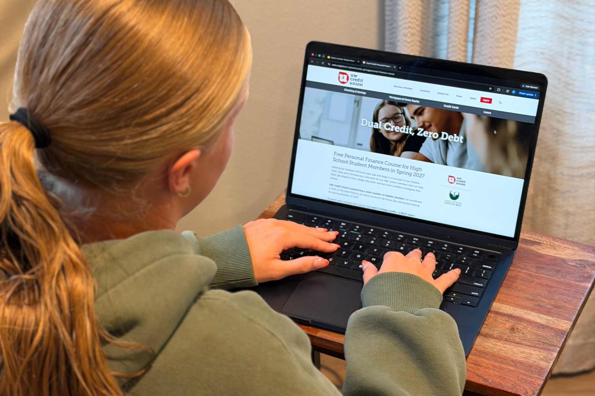 A young woman is pictured from behind as she looks at a webpage on her laptop.