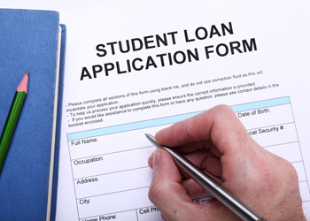 A hand holds a pen while filling out a student loan application form.