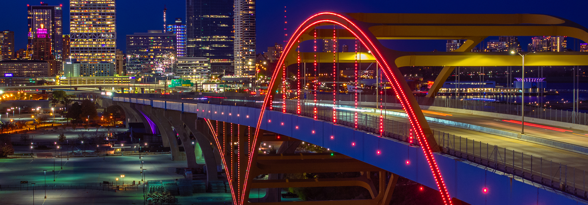 The Hoan Bridge in Milwaukee, Wisconsin pictured lit up at night with the city's' skyline in the background.