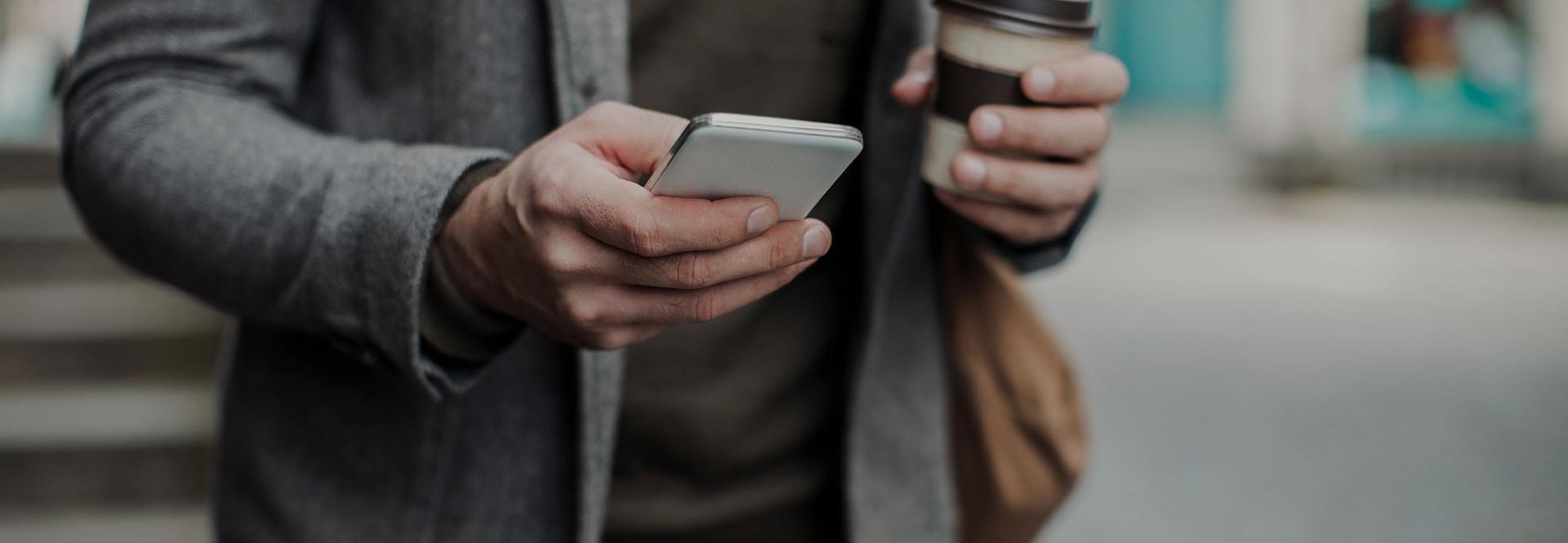 man holding cell phone and coffee